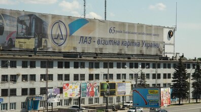 Будівля колишнього ЛАЗу вздовж міської магістралі. На даху споруди розміщений великий банер із написом: «65 років Львівському автобусному заводу. ЛАЗ – візитна картка України», а також зображенням автобуса і логотипом підприємства.