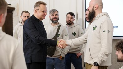Мер Львова Андрій Садовий, у чорному одязі, тисне руку ветеранові у світлому худі. На задньому плані стоять ще кілька ветеранів у подібних худі з логотипами, які спостерігають за розмовою. Позаду видно екран із презентацією.