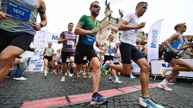 Учасники масового забігу зі стартовими номерами біжать брукованою вулицею повз будівлю Львівської опери.