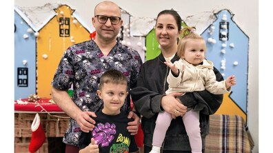 У холі лікарні один біля одного стоять: директор лікарні Олександр Калінчук, пацієнт Давид та його мама, яка тримає на руках маленьку сестричку. Всі усміхнені, а хлопчик показує жест «лайк». На задньому плані – декоративні кольорові будиночки з гірляндами та зимовими прикрасами, а також камін із новорічними шкарпетками.