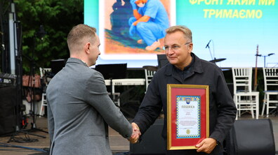 Міський голова під час вручення подяки жме руку капітану медичної служби. На фоні - сцена заходу.
