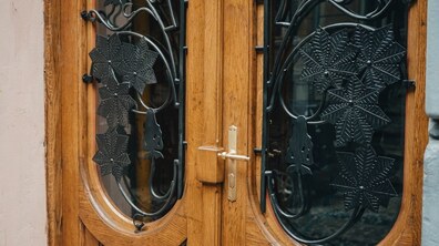 Фрагмент відреставрованої дерев’яної брами із заскленими віконцями, металевою ручкою по центру та кованими решітками з орнаментом із листя каштана.