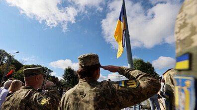 Військові віддають честь під час урочистого підняття Державного Прапора України. На тлі — синьо-жовтий стяг, небо та учасники церемонії.