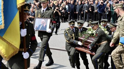 Урочиста похоронна церемонія Степана Кубіва. Військові у парадній формі несуть труну, прикрашену квітами, у супроводі почесної варти. Попереду також несуть портрет і великий синьо-жовтий прапор. На задньому плані помітно велику кількість людей, які прийшли попрощатися та віддати шану нардепу.