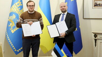 Перший заступник міського голови Львова Андрій Москаленко та заступник міського голови Таллінна Крістіан Ярван стоять і тримають в руках підписаний меморандум, позаду - три великі прапори: український, міста Львова та Європейського Союзу