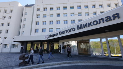 Лікарня святого Миколая. В напрямку від входу межичного закладу йдуть люди. Попереду сім’я з дитиною у візку. На задньому плані видно корпус лікарні. Фото ілюстративне