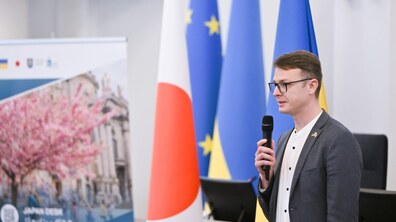 Андрій Павлів - начальник управління інвестицій та проєктів Львівської міської ради, в окулярах, сірому піджаку та білій сорочці, говорить у мікрофон. Він стоїть на тлі прапорів Японії, Європейського Союзу та України. Ліворуч розташований банер із зображенням квітучої сакури та написом «JAPAN DESK»