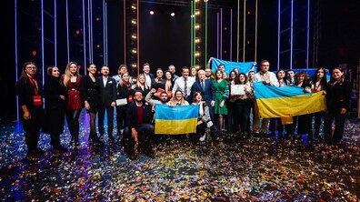 На сцені велика група людей — молодь, організатори та почесні гості. Учасники тримають українські прапори, дипломи та відзнаки, а сцена вкрита різнокольоровим конфеті.