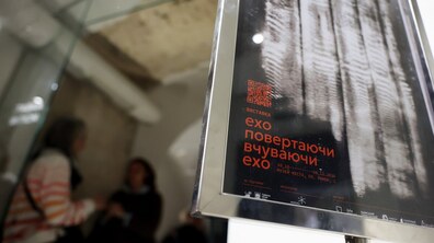 На передньому плані — афіша виставки «Ехо повертаючи, вчуваючи ехо». На задньому плані, у розмитому фокусі, видно двох відвідувачок, які розглядають експозицію