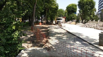 Ремонт вулиці. Збоку лежить на купах бруківка та будівельні матеріали. З іншого боку ростуть дерева та кущі. Їх відгородили сіткою.