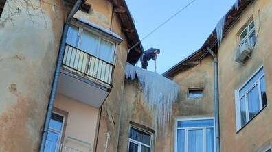 альпініст збиває величезні крижані бурулі з даху житлового будинку