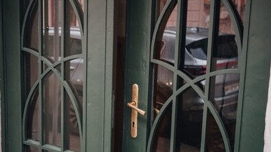 Фрагмент відреставрованої брами темно-зеленого кольору. Двері мають великі скляні вставки з витонченим декоративним переплетенням. У склі відображається вулиця та автомобілі.
