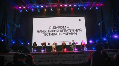 Спікери під час панельної дискусії сидять на сцені. Позаду на екрані напис
