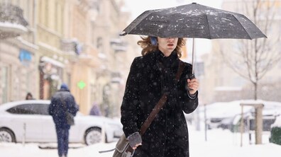 Дівчина йде засніженою вулицею з парасолею в руці. Падає сніг