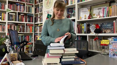 Ілюстративне фото. Молода жінка стоїть біля стосу різних книг, розгорнувши найвищу з них, читає