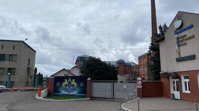 ворота, які ведутьна територію комплексу та будівля з червоної цегли на фоні похмурого нема з вивіскою «Львівський лікеро-горілчаний завод»