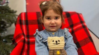 Маленька пацієнтка Марічка сидить у кріслі, накритому яскравим червоно-чорним пледом. Вона сором’язливо усміхається, її темно-русяве волосся зібране у два хвостики. Дівчинка одягнена у блакитну сукню, а в руках тримає в’язану іграшку – ведмедика. Позаду стоїть новорічна ялинка