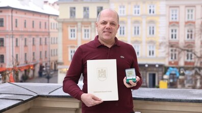 Працівник міського управління соціального захисту Іван Фасольник на балконі міської Ратуші. У руках він тримає подарунки для довгожителів - вітальний лист від мера та пам'ятну монету.