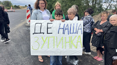 Мешканці Гряди стоять на дорозі біля свого села. По центру хлопець тримає у руках плакат з написом “Де наша зупинка”
