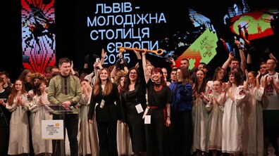 На фото — велика команда молоді на сцені святкує титул «Львів — Молодіжна столиця Європи 2025». У центрі учасники тримають символічний золотий ключ, а позаду на екрані видно назву події.