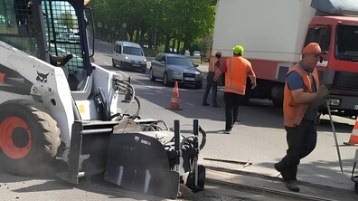 Ремонт на вул. Левандівській. Працює спецтехніка, а поруч працюють дорожники у помаранчевих жилетах. На задньому плані — вантажівка, автомобілі та дерева вздовж вулиці.