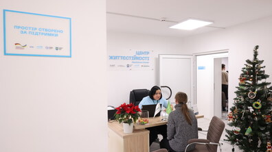 Працівниця Центру життєстійкості консультує відвідувачку - обоє спілкуються, сидячи за столом; біля столу стоїть новорічна ялинка, на стіні - табличка з назвою центру та донорами, завдяки яким відкрили центр