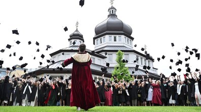 На фоні храму сотні студентів у мантіях підкидають вгору квадратні академічні шапки
