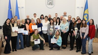Близько двох десятків учасників програми “Відвага до бізнесу” з сертифікатами в руках разом з представниками Львівської міськради та партнерами у Великій сесійній залі Ратуші. Позаду них прапори: ЄС, України та міста, а на стіні Герб Львова