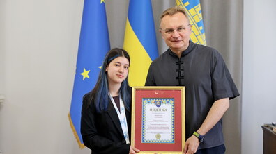 Міський голова Львова Андрій Садовий поруч з шахісткою Анастасією Гнатишин тримають у руках відзнаку від міста. Позаду видно прапори ЄС, України та Львова.
