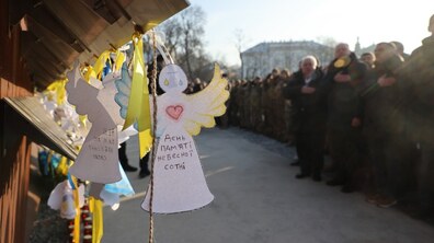 На передньому плані великим планом зображено паперового ангела з написом «День пам'яті Небесної Сотні». У глибині кадру, на алеї, вишикувалася шеренга людей та військових у формі, які тримають праву руку на серці під час урочистого вшанування пам'яті