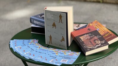 На круглому зеленому столику розкладено книжки різних видавництв, серед яких виділяється розгорнута збірка «4.5.0. Антологія воєнної літератури». Поруч лежить стопка яскравих блакитних флаєрів із написом «Форум видавців у Львові».