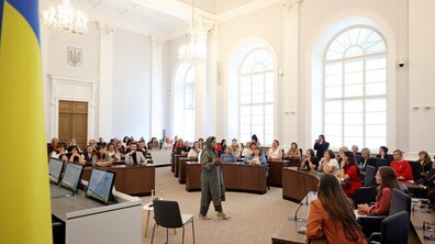 У великій сесійній залі ЛМР перед вчителями виступає сестра Зеф. На передньому плані зліва видно частину українського прапора.