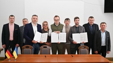 по центру Микола Гандера, радник з технічних питань будівництва GIZ, Андрій Москаленко, перший заступник міського голови Львова, Julian Bihl, генеральний директор IBS GmbH тримають підписаний меморандум про співпрацю. Позаду них стоять депутати і міські посадовці.