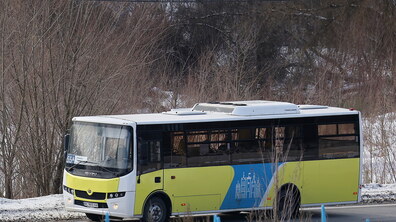 Автобус середнього класу у жовто-блакитних кольорах проїжджає повз безлисті дерева. На його борті зображено логотип Львова.