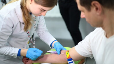 Медична працівниця у рукавичках бере кров у пацієнта: момент, коли кров голкою поступає у спеціальний контейнер для забору крові