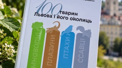 На фото зображено обкладинку посібника «100 тварин Львова і його околиць», на якій стилізовано силуети різних тварин. Книжка на тлі зеленої рослинності та міського пейзажу