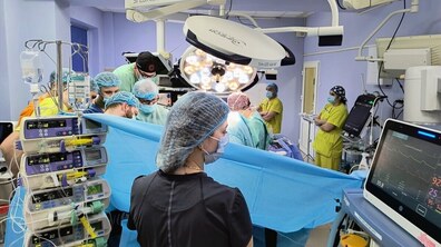 Операційна під час хірургічного втручання. Команда медиків у стерильному одязі, масках і шапочках працює біля пацієнта під яскравим операційним світлом. Навколо видно сучасне медичне обладнання – монітори, інфузійні насоси та апаратуру для контролю стану пацієнта.
