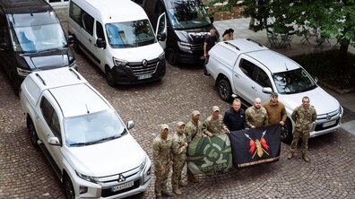Андрій Садовий та військовослужбовці поруч із п’ятьма автомобілями – мікроавтобусами та пікапами у внутрішньому дворі Ратуші. Військові тримають два прапори з емблемами своїх підрозділів, а позаду них стоять мікроавтобуси та пікапи, які місто передає для фронту.