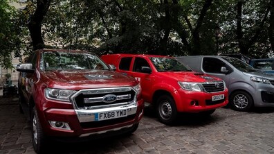 Кілька різних автівок стоять у ряд на одній з вулицб Львова
