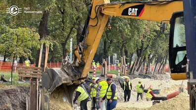 Масштабні ремонтні роботи на вул. Мазепи: група робітників у світловідбивальних жилетах працює на проїзній частині поруч із великим екскаватором. Уздовж дороги видно дерева та іншу будівельну техніку