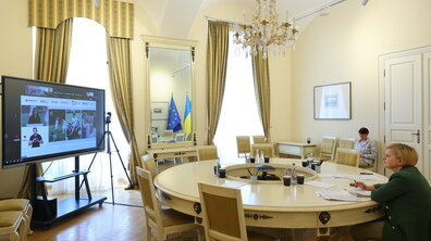 Зала засідань у класичному стилі, де за круглим столом сидить Ірина Маруняк – заступниця міського голови Львова з питань доступності, яка онлайн долучилася до засідання Ради Безбар’єрності. Ліворуч встановлено великий екран, на якому видно онлайн-конференцію.
