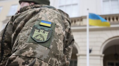 Рука військового з нарукавним знаком Державний Прапор України та нарукавним знаком військової частини на фоні Державного Прапора України на флагштоку діля Львівської міської ради