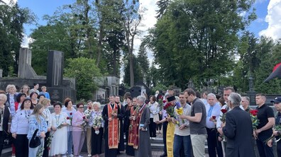 На Личаківському цвинтарі науковці, духовенство та представники міста зібрались, щоб вшанувати пам'ять діячки ОУН Ірини Сеник. Вони мають в руках червоні троянди та блакитно–жовті квіти. Люди одягнені у вишиванки