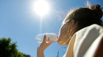 Жінка п’є воду з пластикової пляшки на відкритому повітрі в дуже сонячний день. Яскраве сонце світить високо в небі.