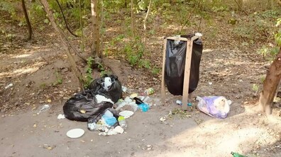 Ілюстрація безвідповідального відпочинку: у парку поміж зелених дерев розкидане сміття. Декілька розірваних чорних поліетиленових пакетів на землі