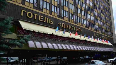 На фото зображено львівський готель “Дністер”. Над входом висять прапори різних країн. Поруч припарковані авто