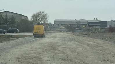 Вул. Конюшинна з нерівною дорогою без покриття, що веде у промислову зону. Вдалині видно яскраво-жовтий вантажний мікроавтобус. Праворуч видно сірі промислові склади, обгороджені парканами.