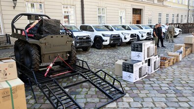 На брукованому подвір’ї стоять кілька нових білих пікапів, різні коробки з технічним обладнанням. Поруч зібралися військові й цивільні.