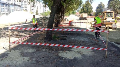 Ділянка вул. Мазепи, де тривають ремонті роботи. Частина огороджена сигнальною стрічкою. Поруч працюють дорожники у світловідбивних жилетах, а на задньому плані видно будівельну техніку та насипи будівельних матеріалів.