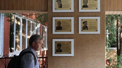 П'ять меморіальних таблиць захисникам на фасаді однієї з міських шкіл. Біля них стоїть сивочолий чоловік із задуманим поглядом. Фото ілюстративне